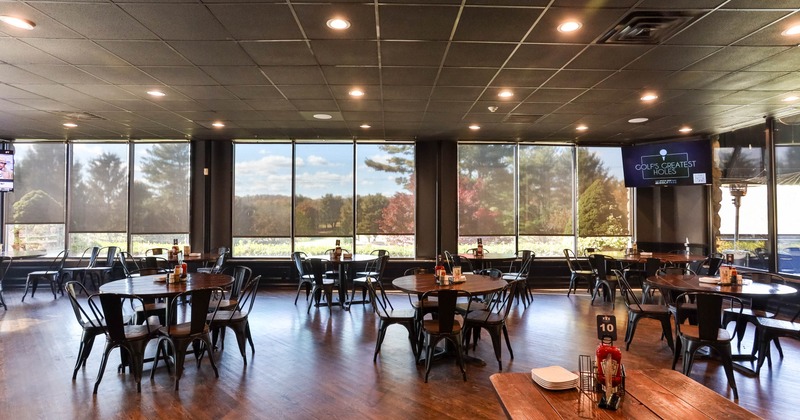 Dining area with large windows, round wooden tables, metal chairs, and a mounted TV