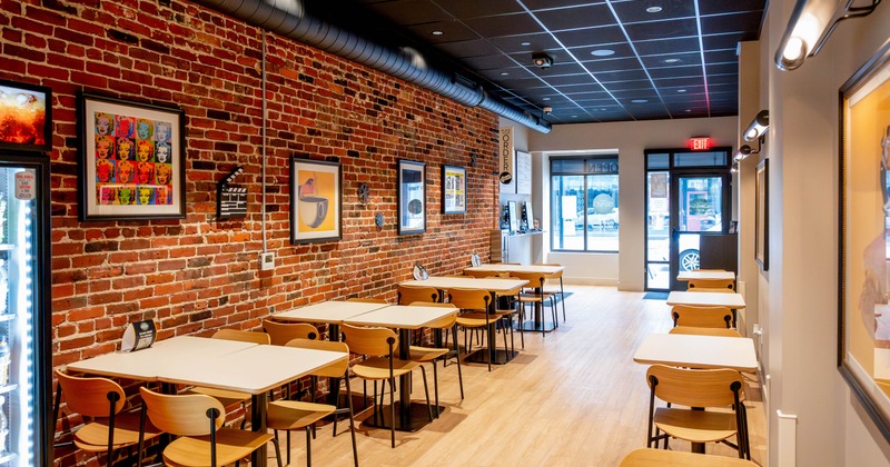 A cafe with exposed brick walls, light wood tables and chairs, and framed artwork