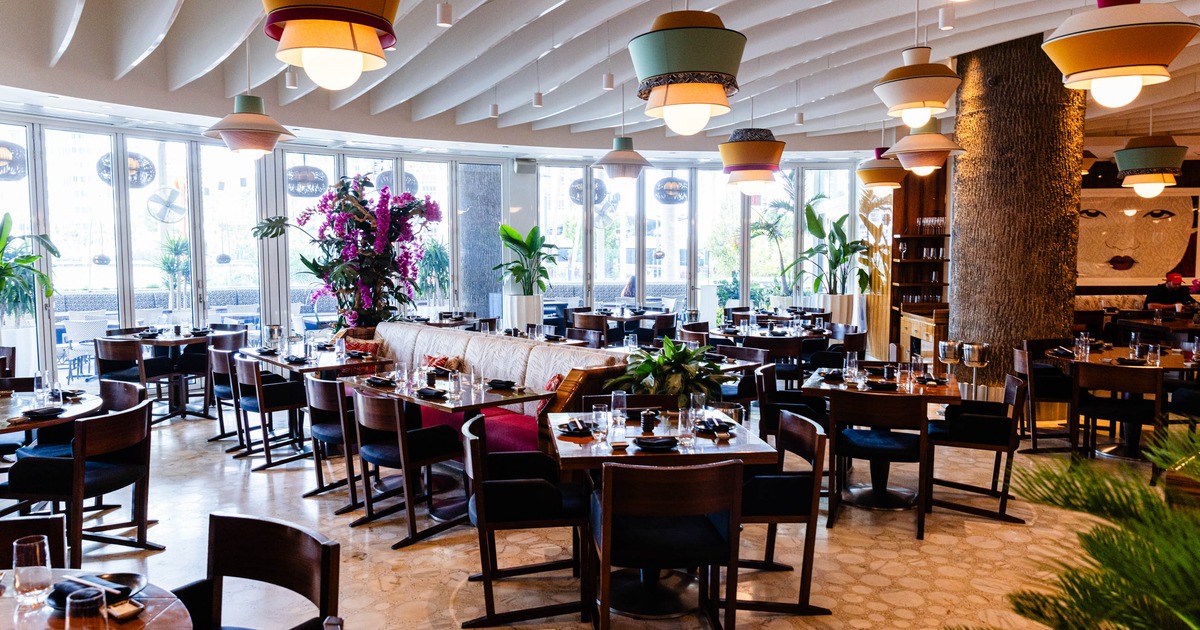 A modern interior - wooden tables, colorful pendant lights, decorative plants, large windows