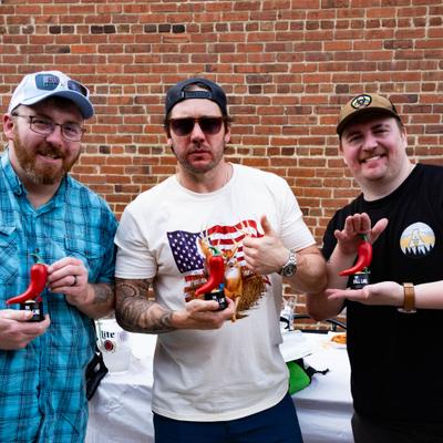Three persons posing outdoors with chili cook-off trophies.