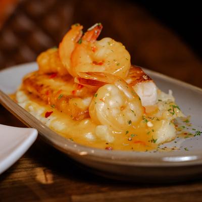 A dish of grilled mahi mahi topped with shrimps, with tomato sauce, yuca, and rice.