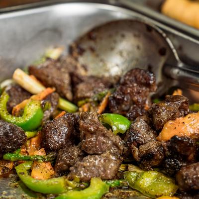 Stir-fried beef chunks with green bell peppers and carrots in a tray.