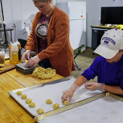 Two people preparing chocolate chip cookie dough for baking.