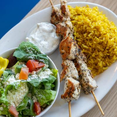 Grilled chicken skewers served with yellow rice, tzatziki, and a side salad.