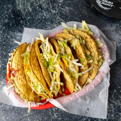 A red basket lined with paper holding several tacos topped with lettuce.