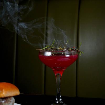 Red cocktail with rosemary garnish.