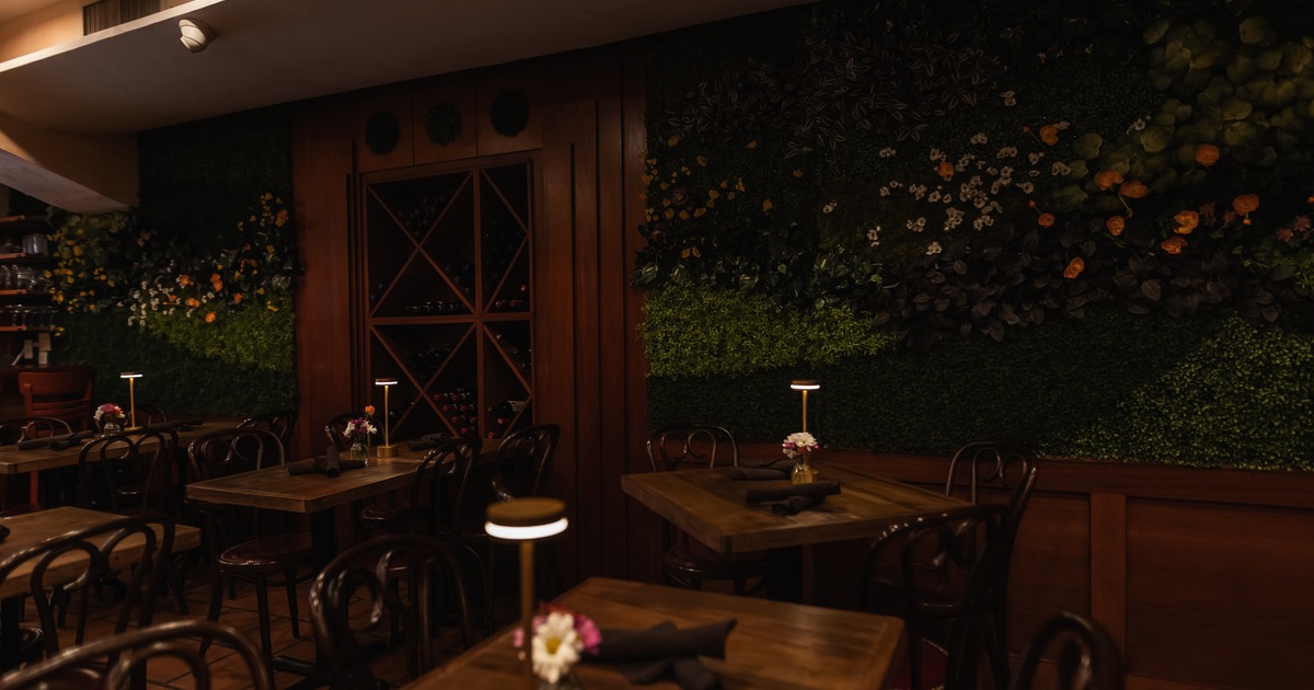 Dimly lit seating area with wooden tables and a green flower wall