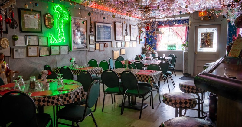 Interior of a restaurant with checkered tablecloths, green neon Italy sign