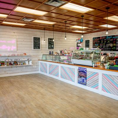 Interior featuring a counter, glass display cases, menu boards, and a pink neon sign.
