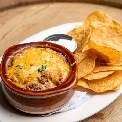 Baked chili served with chips and dipping sauce on a wooden surface.