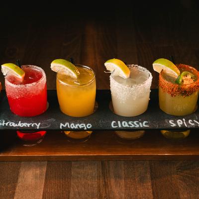 Margarita flight with four different cocktails and labels on a wooden tray.