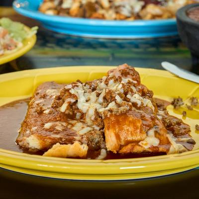 Tamales topped with brown sauce, melted cheese, and ground meat.