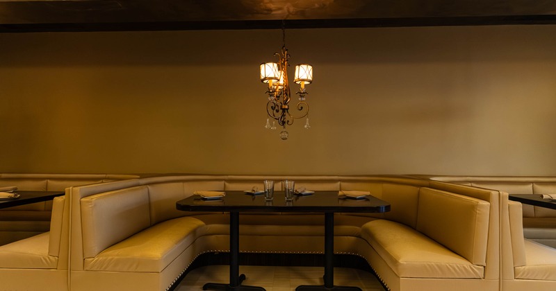 A tan leather U shaped booth with a dark wooden table and chandelier in a restaurant