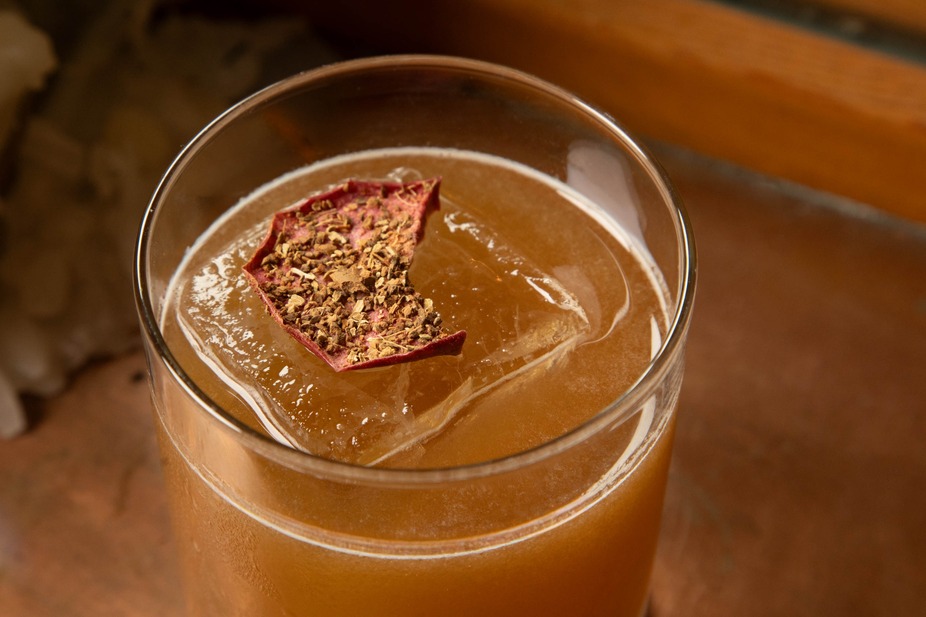 Cocktail with an ice cube, dried rose petal, and spice