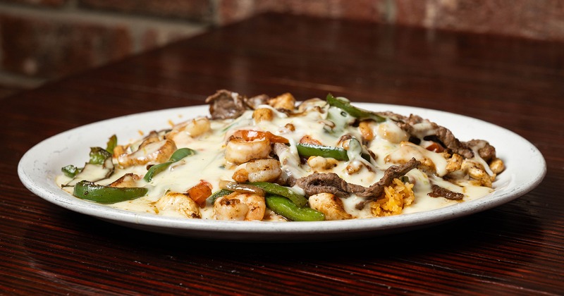 A white plate holds grilled steak, shrimp, and vegetables covered in melted cheese