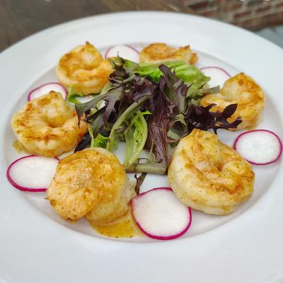 Seared shrimp arranged on a plate with greens and radish slices.