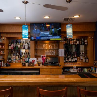 Wooden bar with shelves of liquor, blue pendant lights, and TV.