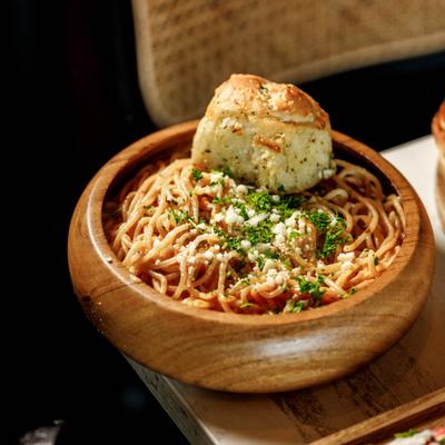 Spaghetti marinara served with garlic bread in a wooden bowl.