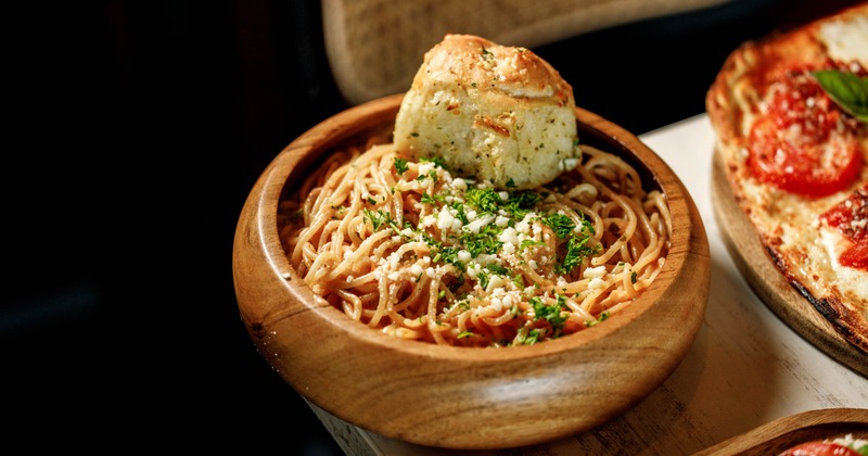 A wooden bowl filled with spaghetti topped with herbs and garlic bread