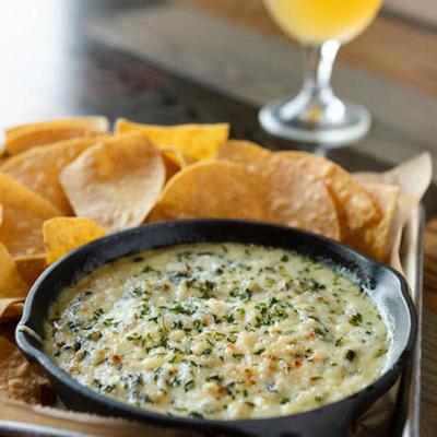 Cheese, spinach, and artichoke dip, with tortilla chips on the side.