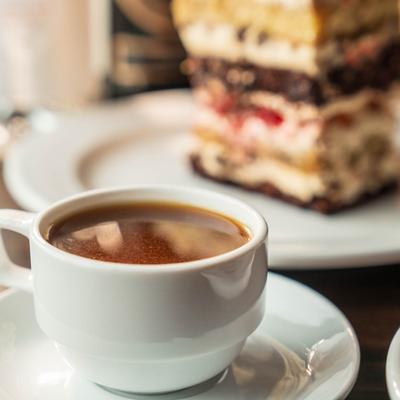 Cup of Turkish coffee served on the table with a dessert in the background.