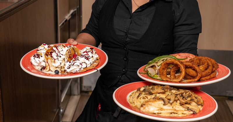 A server holds plates filled with a variety of restaurant dishes