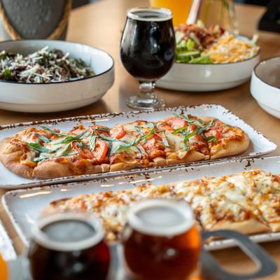 Two distinct flatbreads served served alongside craft beers and bowls of salad.
