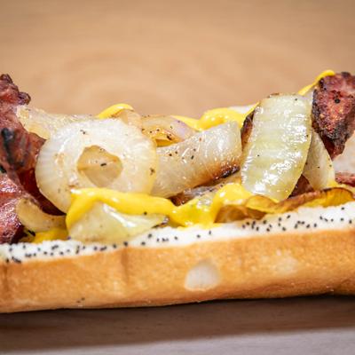 Hot dog with bacon, onions, mustard, and poppy seeds, close-up.