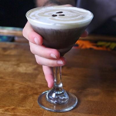 Espresso Martini placed on a bar counter by a bartender, hand shot.