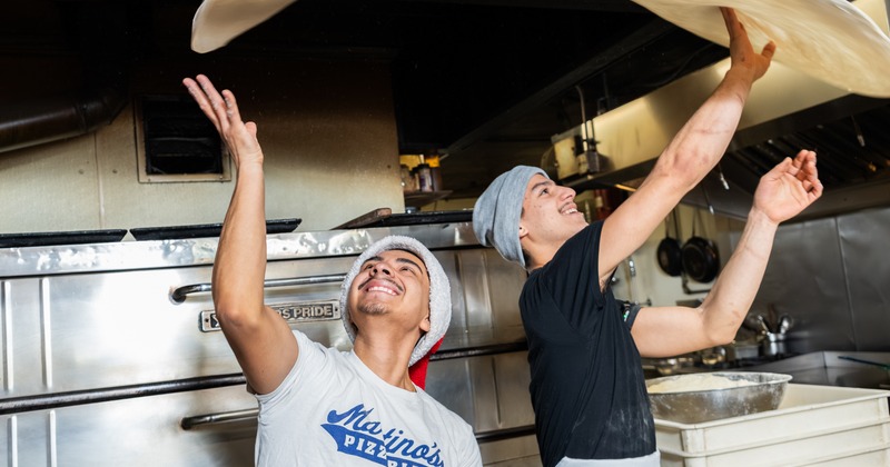 2 pizza masters toss the dough together