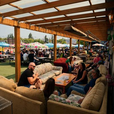 People relaxing on mismatched couches and wooden tables under a covered patio.