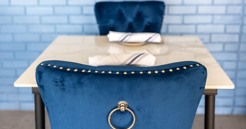 Blue velvet chair with brass accents facing a white marble table with napkins.