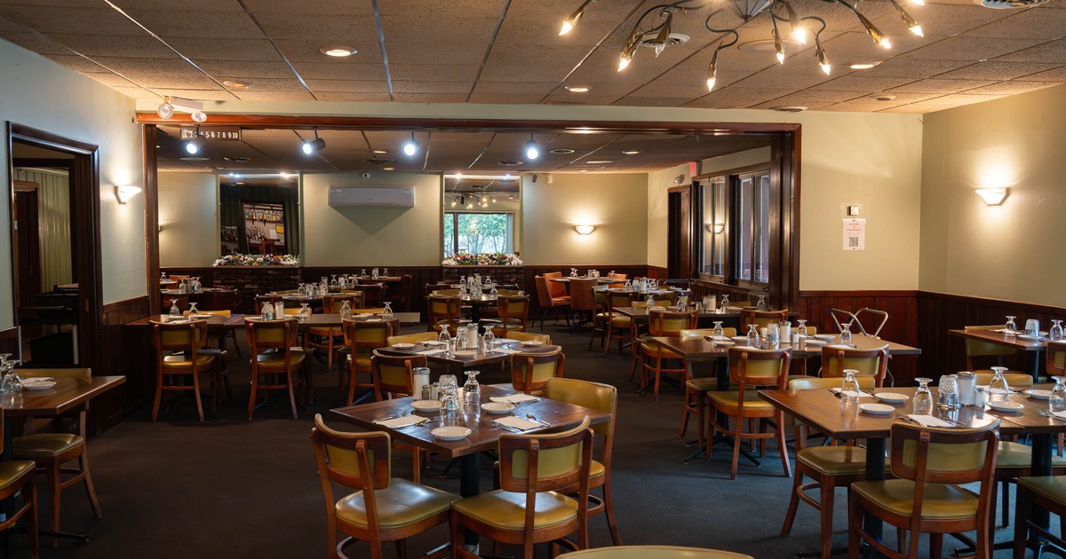 A warmly lit interior - wooden tables and cushioned chairs set with plates and glassware
