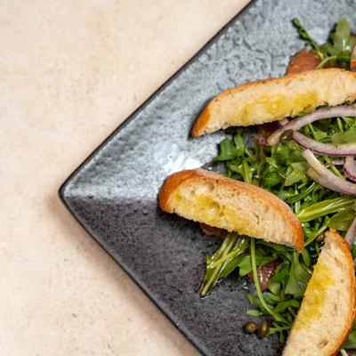 Arugula smoked salmon salad served alongside toasted bread slices on a plate.