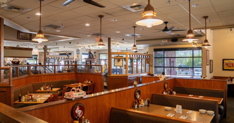 Interior view of a cozy restaurant featuring wooden booths with tables, warm pendant lighting