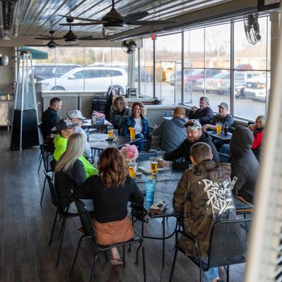 Guests sitting on an indoor-outdoor patio with large windows overlooking a parking lot.