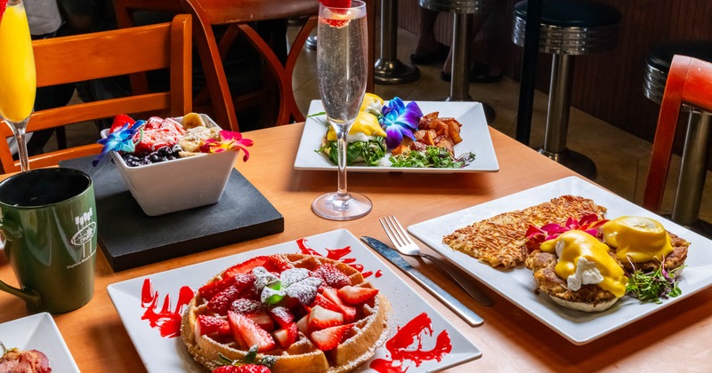Colorful food dishes and drinks spread on a wooden table in a dining setting