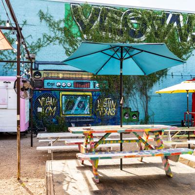 Outdoor seating area with graffiti wall featuring a boombox mural and picnic tables.