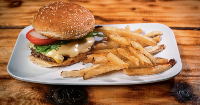 A sesame seed cheeseburger with lettuce and tomato served alongside golden fries