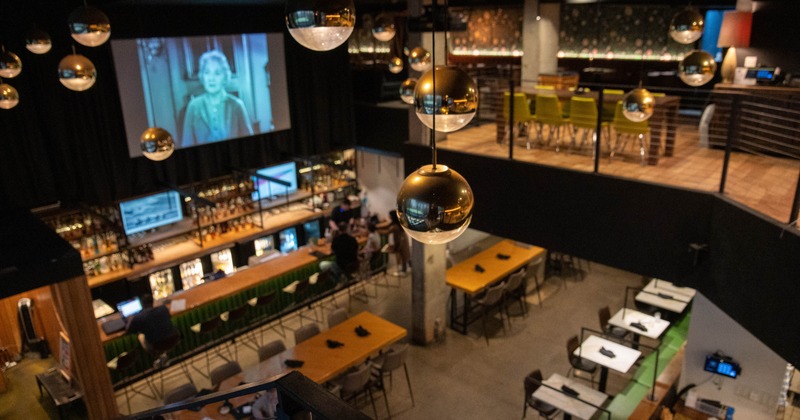A modern bar with a large movie screen and metallic pendant lights