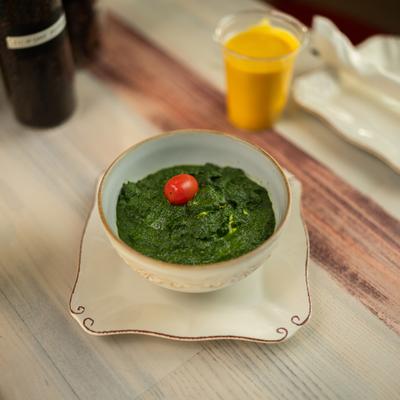 Bowl of spinach paneer topped with a cherry tomato and served with mango lassi.