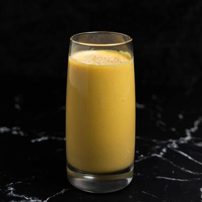Mango lassi in a tall glass on a dark marble surface.