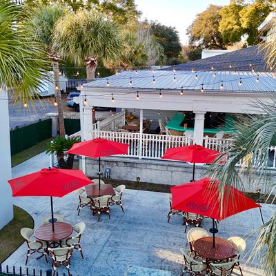 Outdoor patio with red umbrellas and palm trees.