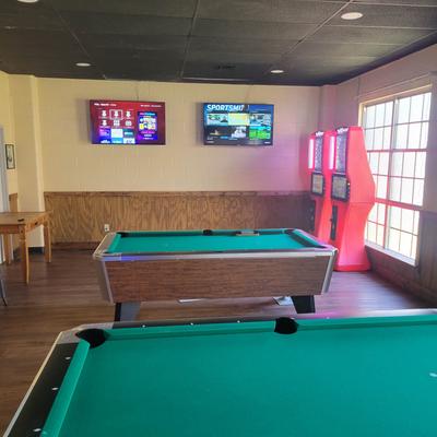 Interior, pool tables and arcade game machines with TV screens on a wall
