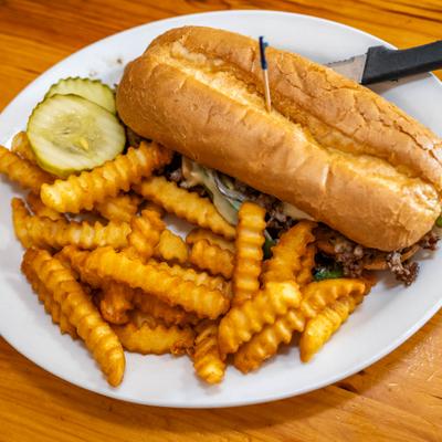 Philly cheesesteak served with crinkle fries and pickle slices.