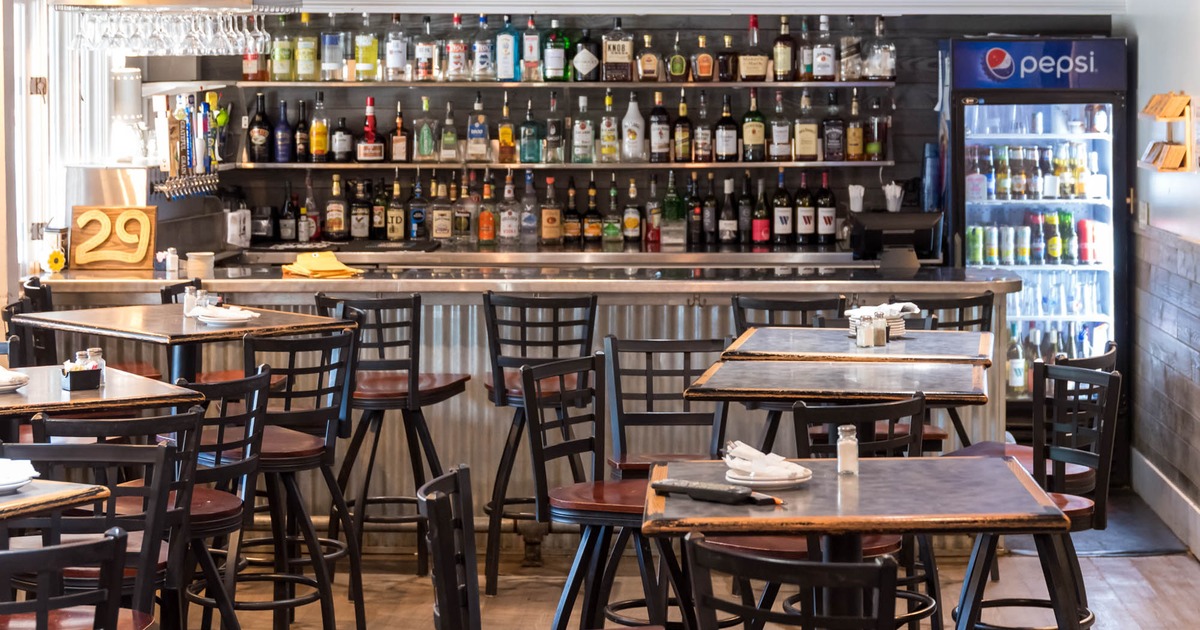 A bar interior with tables, chairs, a stocked bar, and TV.