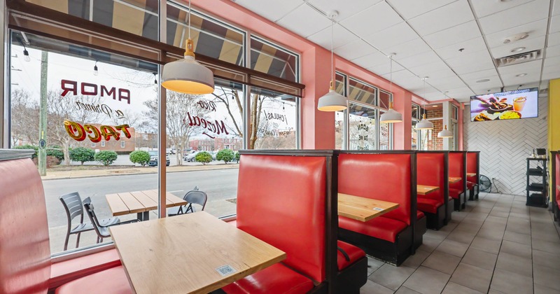 Interior of a restaurant with red booths, wooden tables, and large windows