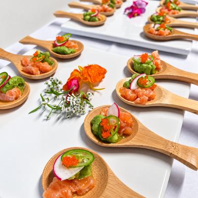 Bite-sized salmon and avocado appetizers served on small wooden tasting spoons.