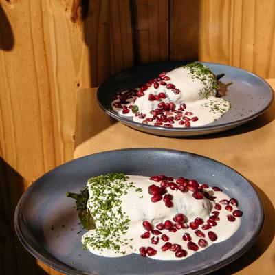 Two plates of stuffed peppers topped with creamy sauce and pomegranate seeds.