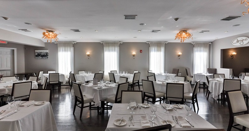 A well-arranged dining room with white tablecloths, elegant chandeliers, and gray walls with windows
